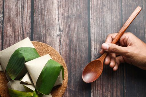 A top view of coconut flavored rice wrapped in banana leaves and a hand holding a spoon