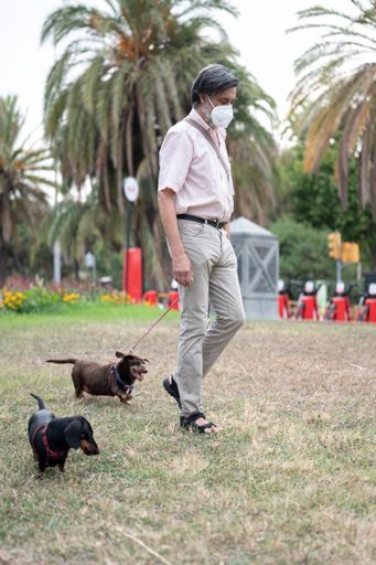 A middle-aged man walking two dogs through the grass of the park in Barcelona