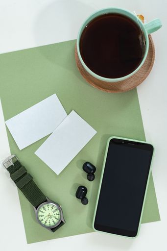 Flat lay of male style accessories with a smartphone, business card, tea cup, watches on green modern office desk