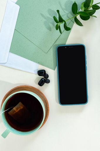 A top view of a smartphone, earphones, paper sheets, and tea cup on green modern office desk