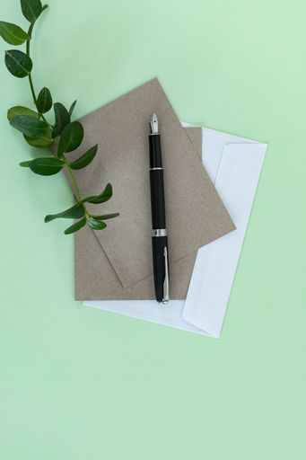 A top view shot of a green surface with an envelope, recycled papers, and a pen