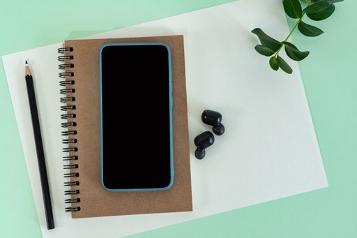 A top view of a smartphone, notebook, pencil, earphones, and paper sheets on a green office desk