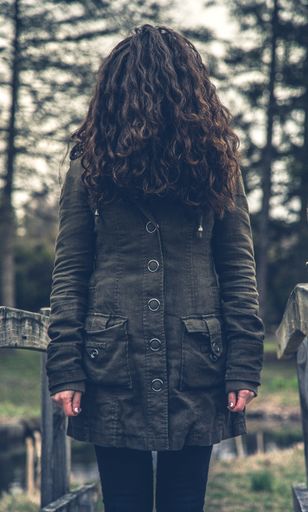 A vertical shot of a female covering her face with hair wearing a raincoat standing on a bridge