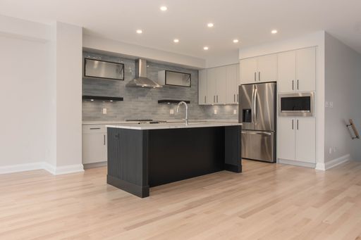 Modern kitchen interior with stainless steel appliances, sleek cabinetry, and a central island, featuring bright lighting and hardwood floors.