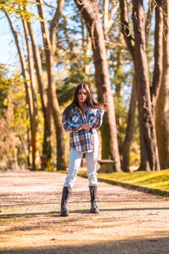 A stylish Caucasian brunette girl in a plaid wool sweater and ripped jeans walking in a park in autumn