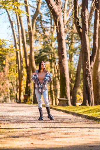 A selective focus shot of  a young caucasian brunette with a plaid shirt and ripped jeans walking in the autumn park