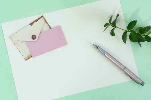 A top view shot of a green surface with papers, an envelope, and a pen