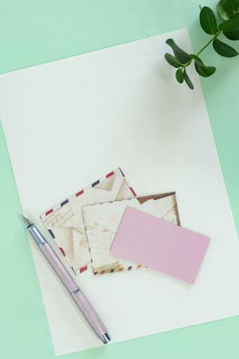 A top view of a business card, envelopes, and a blank paper sheet on a green office desk