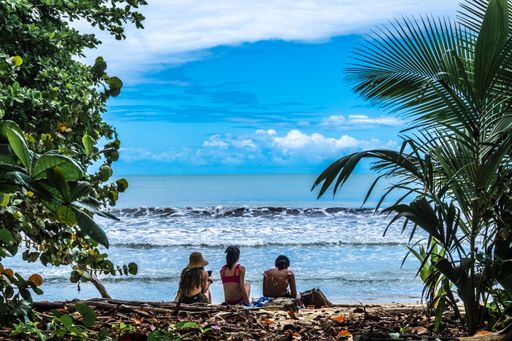 The three girls sitting on a tree log on the sandy beach against the blue seascape in Costa Rica