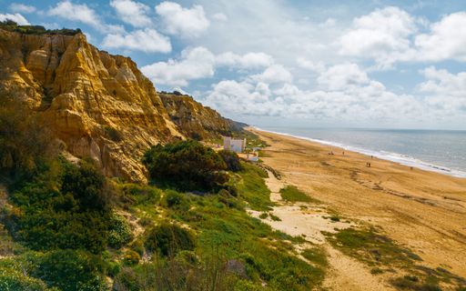 Scenic view of Algarve's golden cliffs and sandy beach under a partly cloudy sky, Portugal.