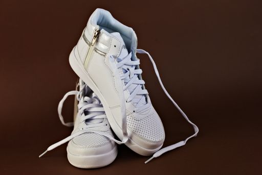 A closeup of white high-top sneakers with untied laces on a brown background.
