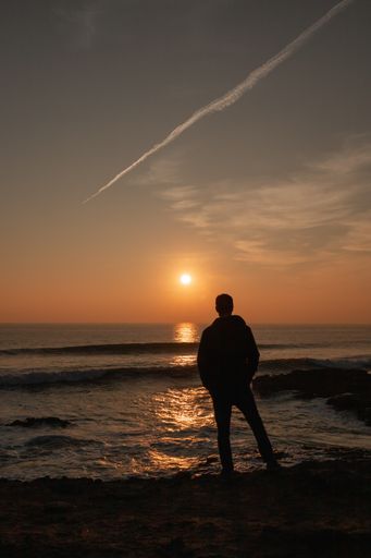 A back view of a man on the beach admiring the beautiful sunset over the Atlantic Ocean in Portugal