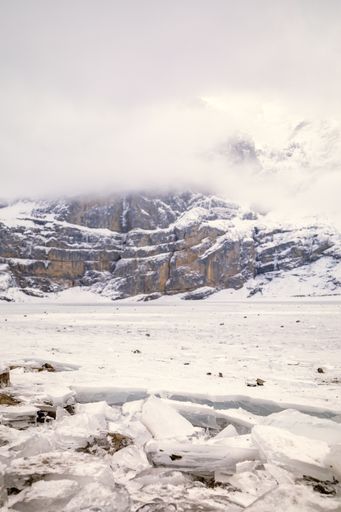 A vertical shot of frozen lake in snowy mountain landscape under dense clouds