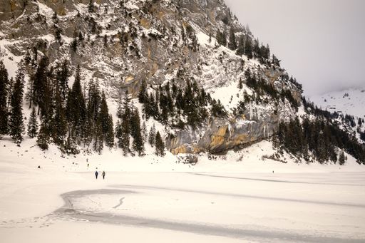 A couple walking on a frozen lake surrounded by the snowy mountains on a cold winter day in Switzerland