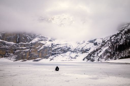 A rear view of female sitting on frozen lake in snowy mountain landscape on a cloudy day