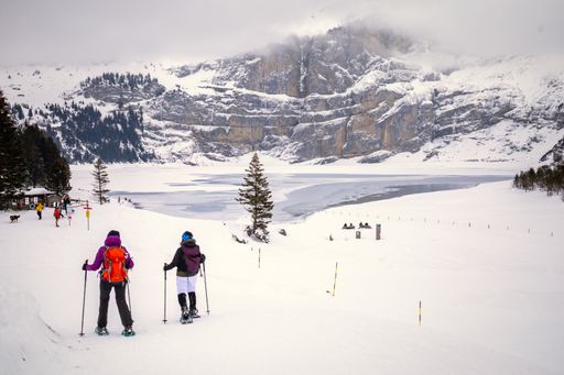The two people walking with snowshoes in snowy mountain landscape with frozen lake on background