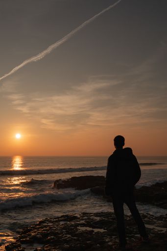A back view of a man on the beach admiring the beautiful sunset over the Atlantic Ocean in Portugal