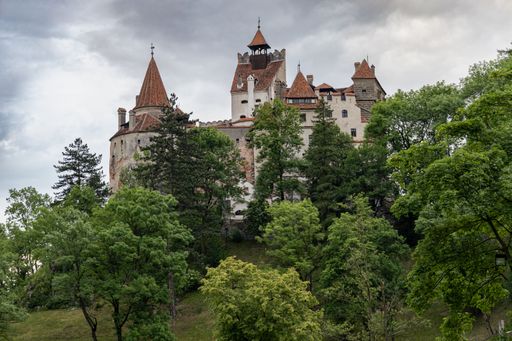 Bran Castle in Transylvania, Romania, surrounded by lush green trees under a cloudy sky.