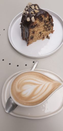 An appetizing coffee with milk accompanied by a piece of chocolate cake with almonds on a white table.