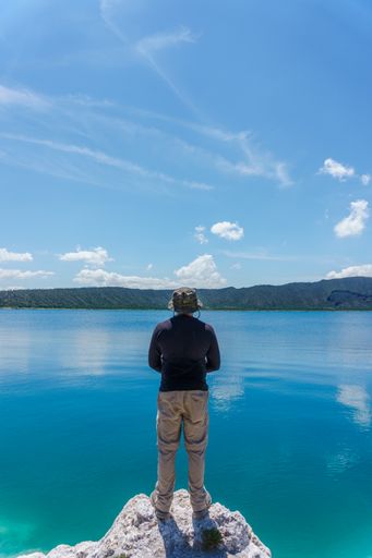 A vertical shot of a Hispanic man standing on the stone with Laguna De San Luis Atexcac on the background