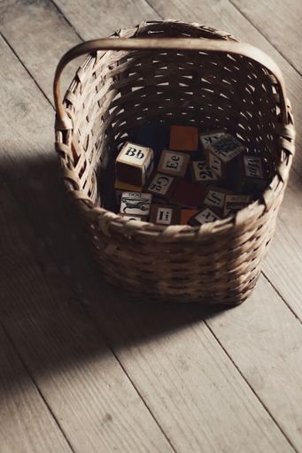A close up shot of a small square letters boxes for teaching kids the letters in a brown basket on a wooden floor