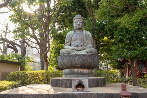A serene Buddha statue in a tranquil garden setting, surrounded by lush green trees and sunlight filtering through the leaves.