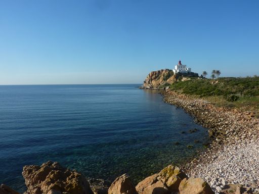 A beautiful view of seashore with a building on a cliff against clear blue sky