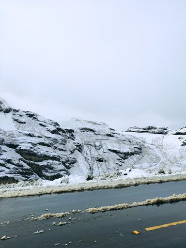 A vertical shot of a wet road by snow-covered rocky mountains under dense clouds in La Cumbre