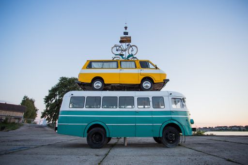 A bust with a van on it and a bicycle on top stacked on each other near the beach