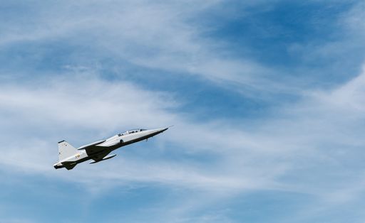 A low angle view of a fighter aircraft flying under a cloudy sky and sunlight at daytime
