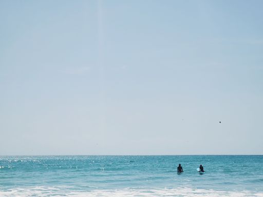 Two surfers in the ocean waiting for waves under a clear blue sky, capturing a serene seascape.
