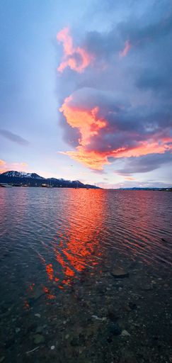 A vertical shot of a colorful seashore during sunset. Ships on mountains background