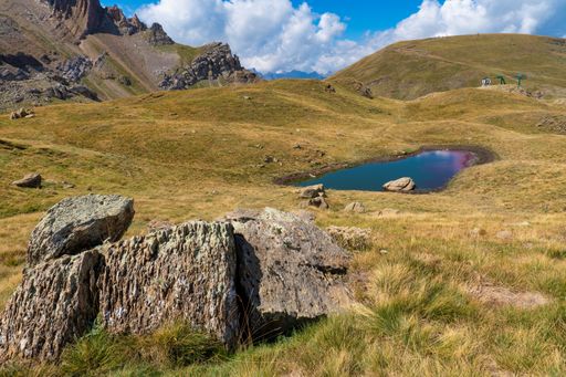 A small lake under a blue cloudy sky in a valley surrounded by mountains on a sunny day