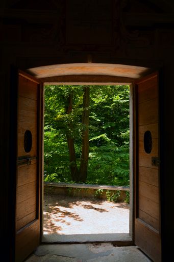 A vertical shot of the double wooden open door leading to the beautiful area with green trees