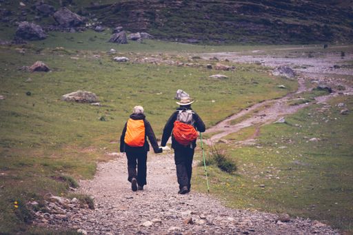 A rearview of an elderly couple hikers with backpacks walking on an unpaved road