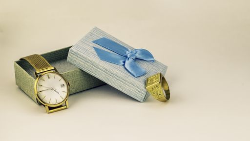A closeup shot of a gold ring and watch near the present box
