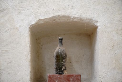 An old dirty damaged glass bottle covered with dust on a piece of brick