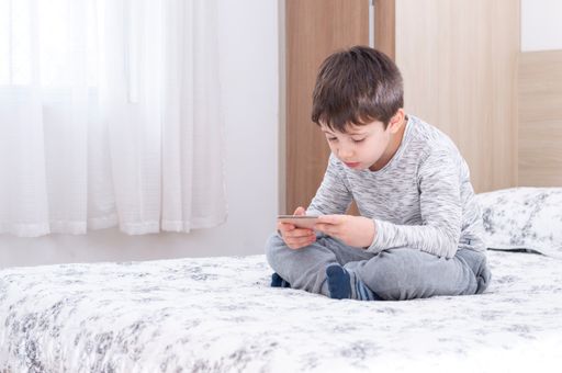Little 6 years old boy using and playing on smartphone. Cute little boy playing games on his smartphone in bed.  Social and technology concept.