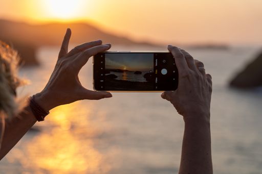 A female tourist taking a picture of the beautiful sunset over the sea with her smartphone
