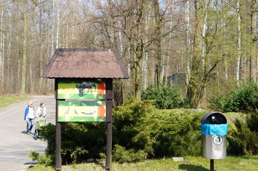A wooden information board showing the direction to animals next to a trash bin in the zoo