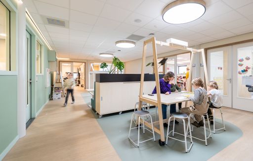 Modern classroom with young children engaged in activities, featuring bright lighting and contemporary furniture.