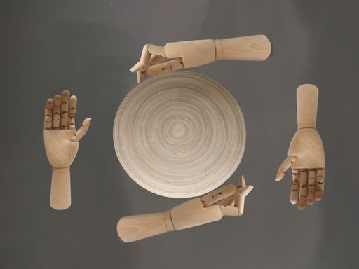 A top view of a round bamboo wooden plate with four wooden hands isolated on gray background