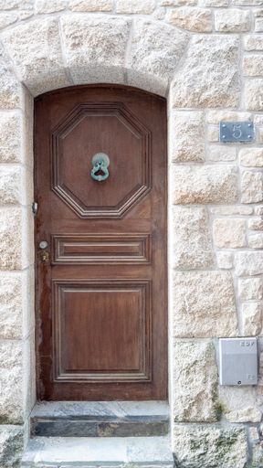 A vertical shot of the old brown wooden entrance house door number five with a metal knocker