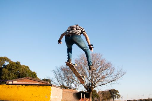 A teen skateboarder doing an allie trick against a blue gradient sky background