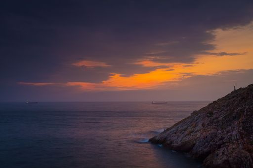 A high angle shot of the rocky cliff by the ocean under the beautiful sunset