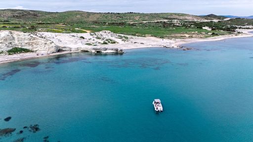 Aerial view of a serene coastline with a boat on turquoise waters and rocky cliffs in the background.