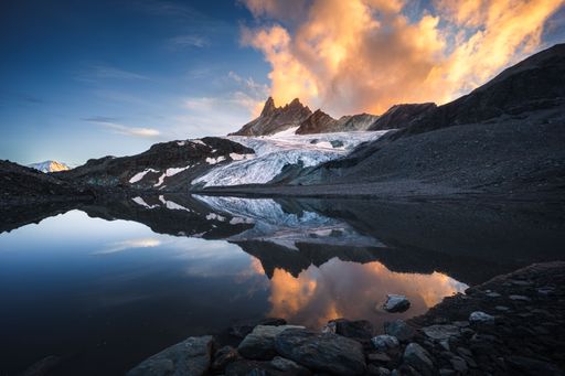 Summer landscape view of the Aiguilles Rouges mountain at sunset with orange clouds and a glacier reflecting in a still lake