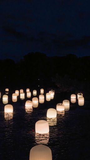 Floating lanterns illuminate a calm river at night, creating a serene and magical atmosphere.