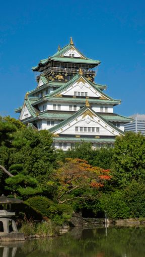 Osaka Castle in Japan with lush greenery and a clear blue sky, showcasing its traditional architecture.