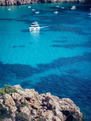 A vertical shot of the beautiful crystal azure water of Ibiza island with ships and boats on a sunny day